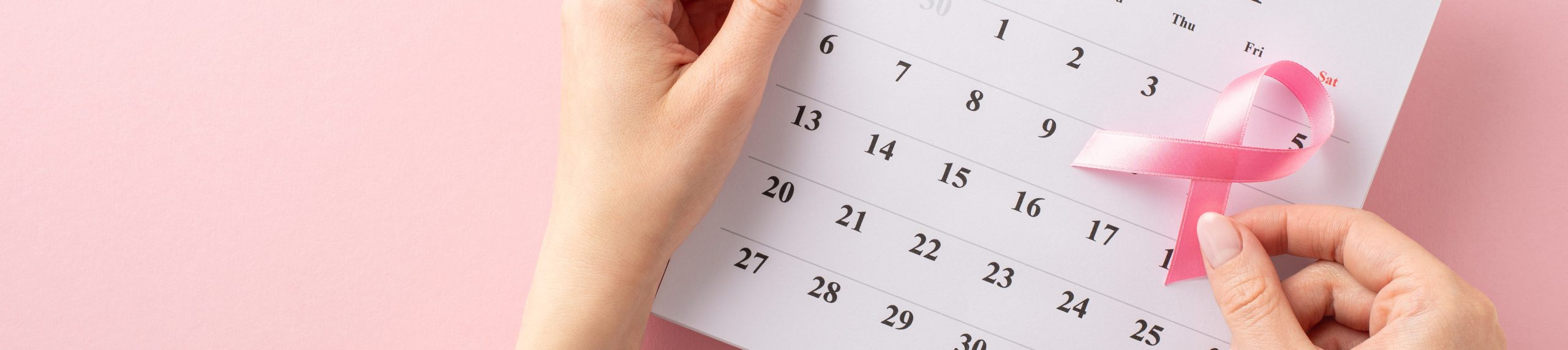 My Breast Cancer awareness setup. First person top view of girl's hands holding October calendar with pink ribbon, gearing up for doctor's visit on pastel pink background with blank area for text