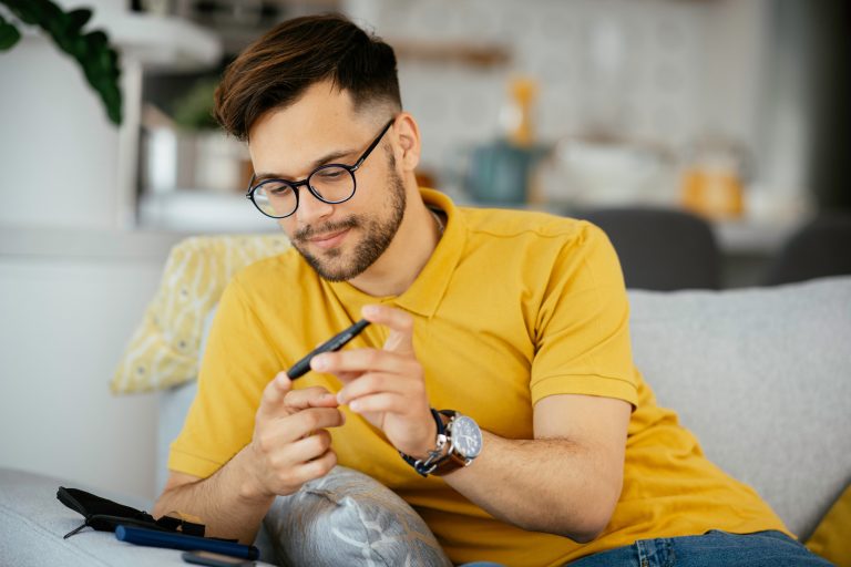 Diabetic man taking blood sample with lancet pen at home