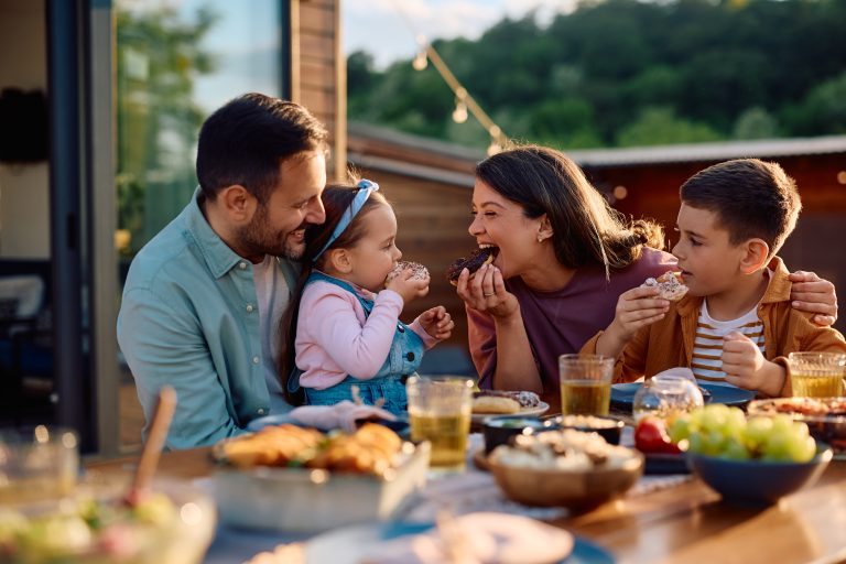Happy family having fun while eating donuts at picnic table on patio